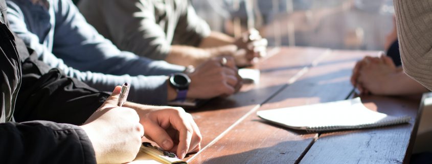 people sitting on chair in front of table while holding pens during daytime