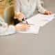 woman signing on white printer paper beside woman about to touch the documents