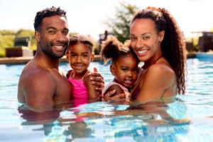 191981199-portrait-family-on-summer-holiday-with-two-girls-being-held-in-swimming-pool-by-parents