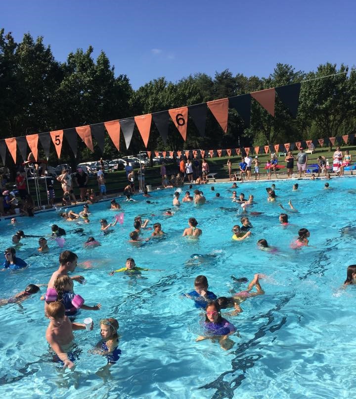 Children and adults playfully swim in a large in-ground pool